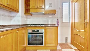 A kitchen with wooden cabinets, a built-in oven, and a window with blinds. - Apartment 'La Bodegueta' with Private Terrace, Wi-Fi and Air Conditioning (Orba)