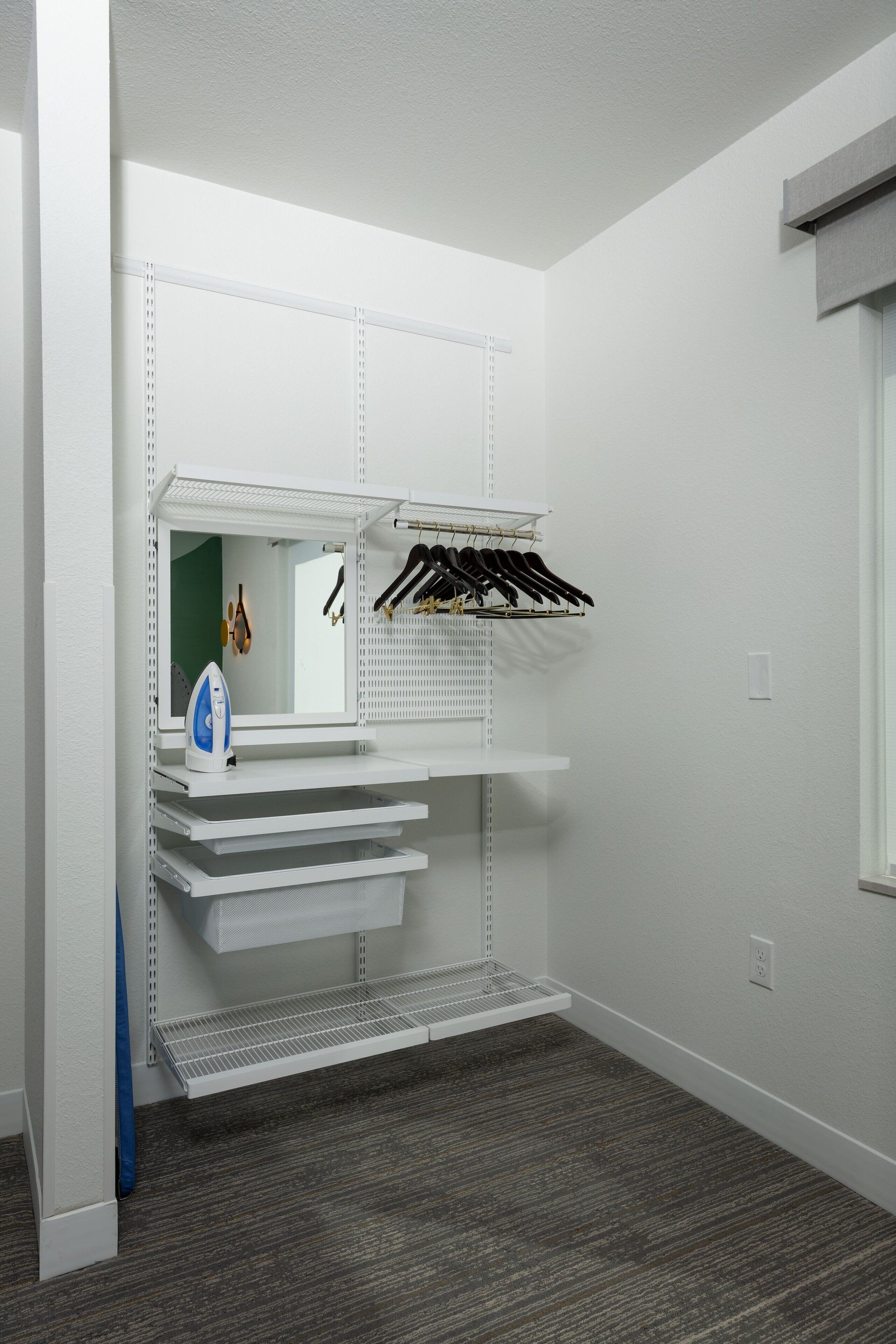 A compact room with a built-in shelving unit, a mirror, and a hanging rack for clothes.