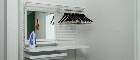 A compact room with a built-in shelving unit, a mirror, and a hanging rack for clothes.