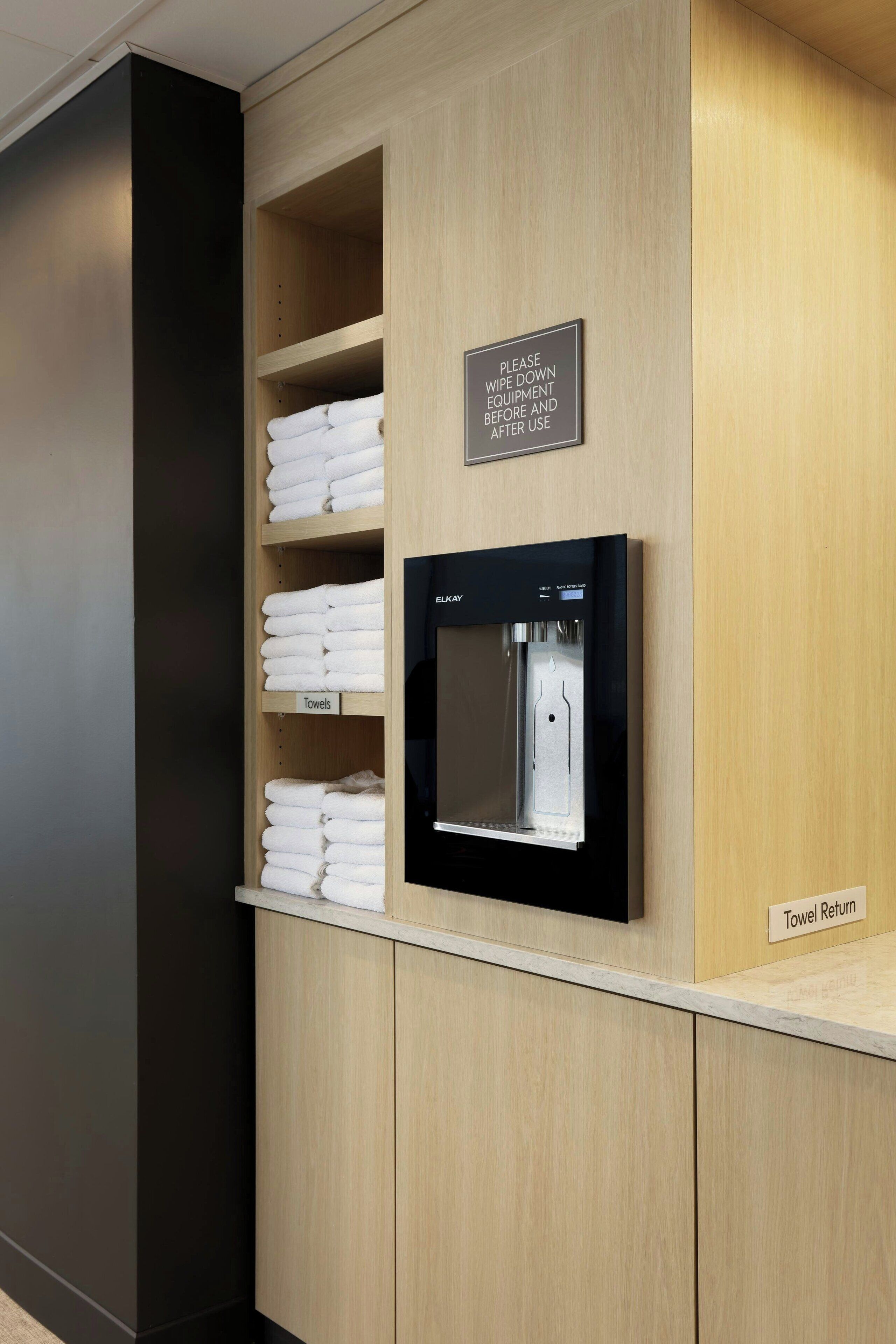 A hotel reception area with a towel dispenser and a sign instructing to wipe down equipment before and after use.
