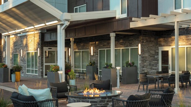 An outdoor patio with stone walls, wicker furniture, and a central fire pit. - TownePlace Suites by Marriott Denver North/Thornton (Thornton)