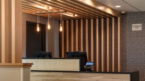 A reception desk with a modern design, featuring a wooden panel wall and a patterned wallpaper. - TownePlace Suites by Marriott Denver North/Thornton (Thornton)