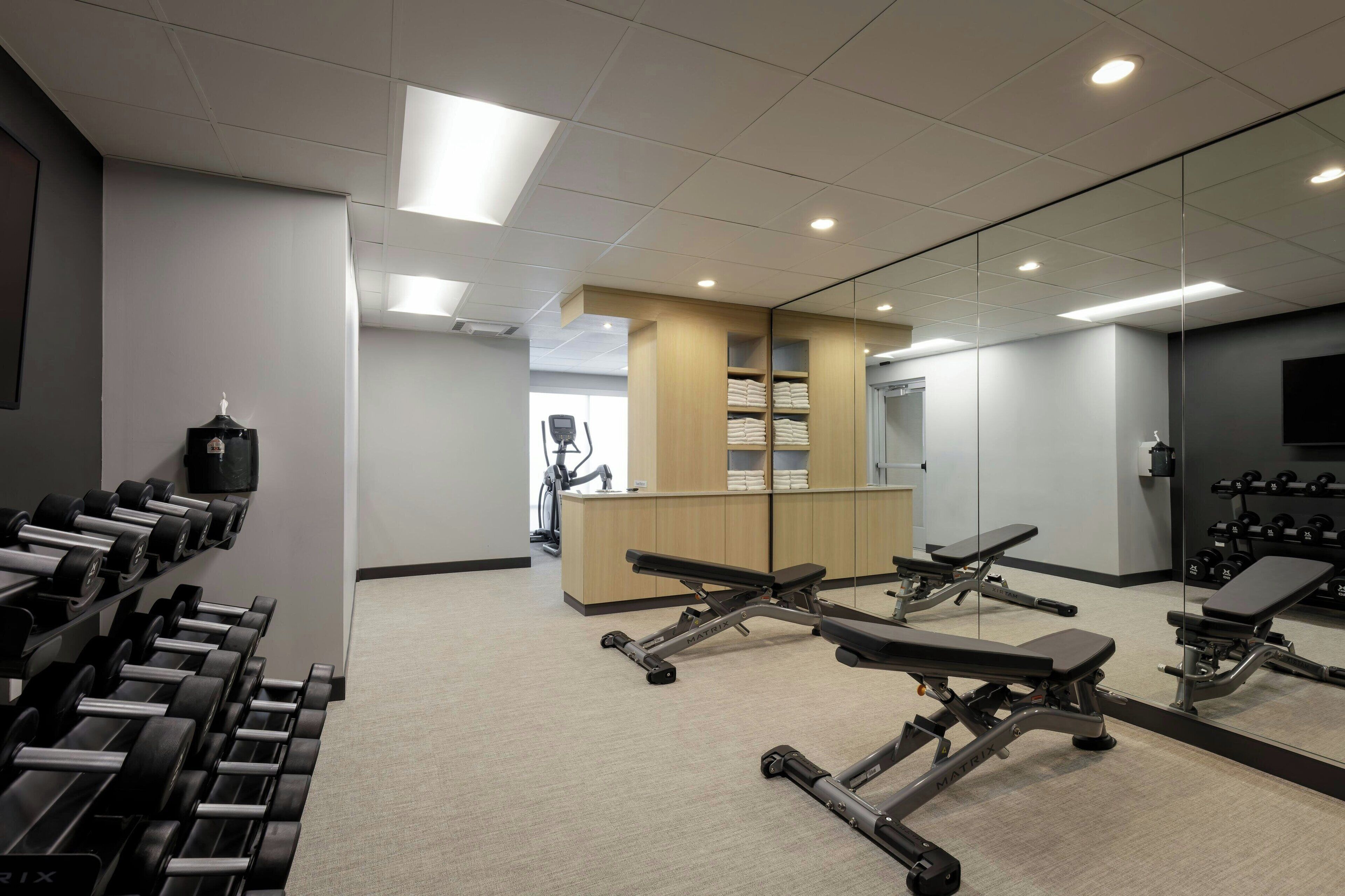 A gym with exercise equipment, a mirrored wall, and a bench.