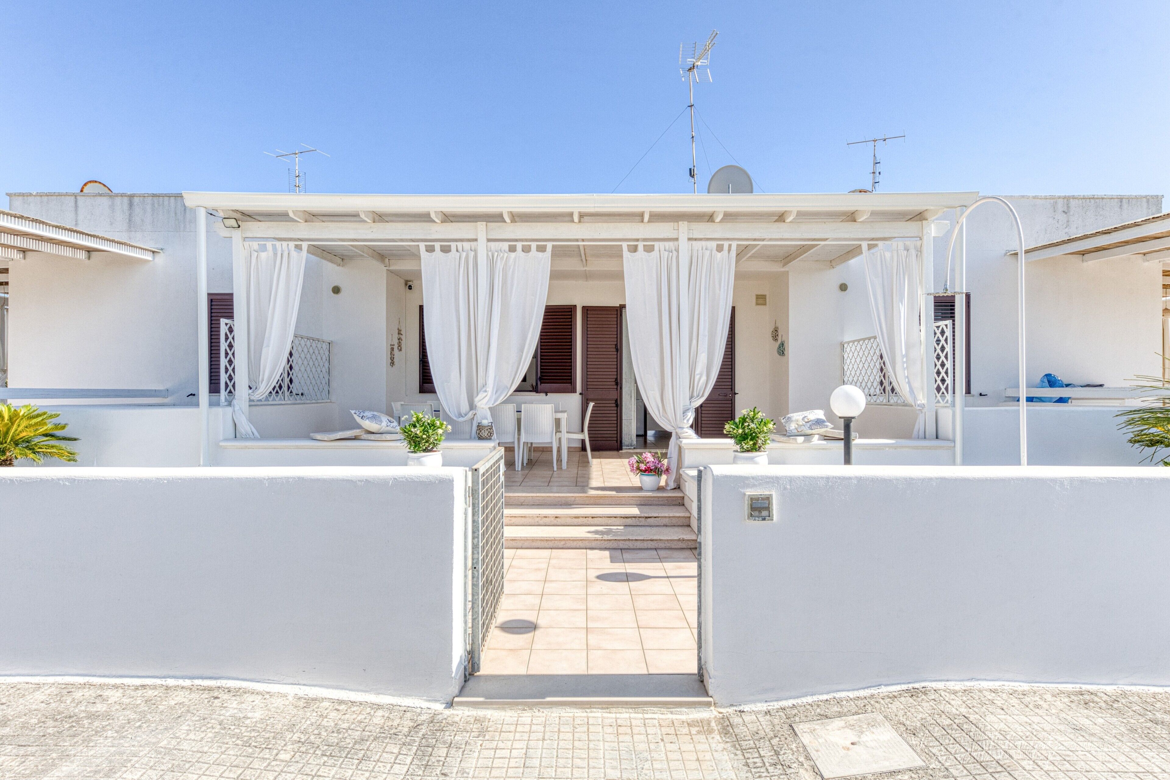 A covered outdoor seating area with a table and chairs, a small garden, and a clear sky.
