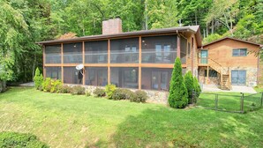 A two-story building with large windows and a balcony, surrounded by a well-maintained lawn and trees. - Peaceful, Spectacular Views, Screened Porch (Franklin, NC 28734)