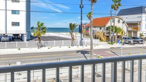 Una calle costera con un edificio blanco, palmeras y una playa al fondo.