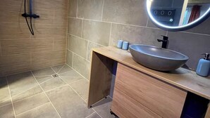 Un bany modern amb un lavabo gran de superfície, un moble de tocador de fusta i un vàter de dutxa manual.