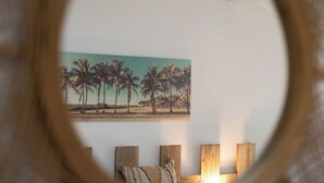 Une chambre avec un tableau représentant des palmiers accroché au mur, une tête de lit en bois et une lampe de chevet.