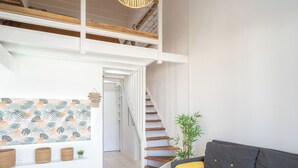 Un salon moderne avec un canapé gris, une table basse ronde en bois et un escalier menant à un niveau supérieur.