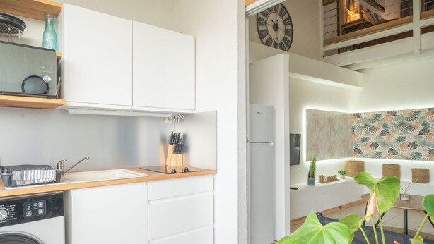 Une cuisine moderne avec des meubles blancs, un lave-linge encastré et une horloge au mur.