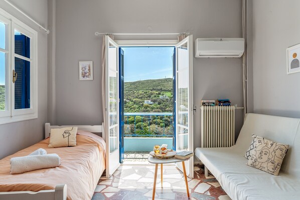 A bedroom with a bed, a sofa, a small table, and a view through an open door.