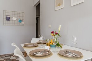 A dining table set for four with placemats, cutlery, and wine glasses. There is a small vase with flowers and a bowl of lemons on the table.