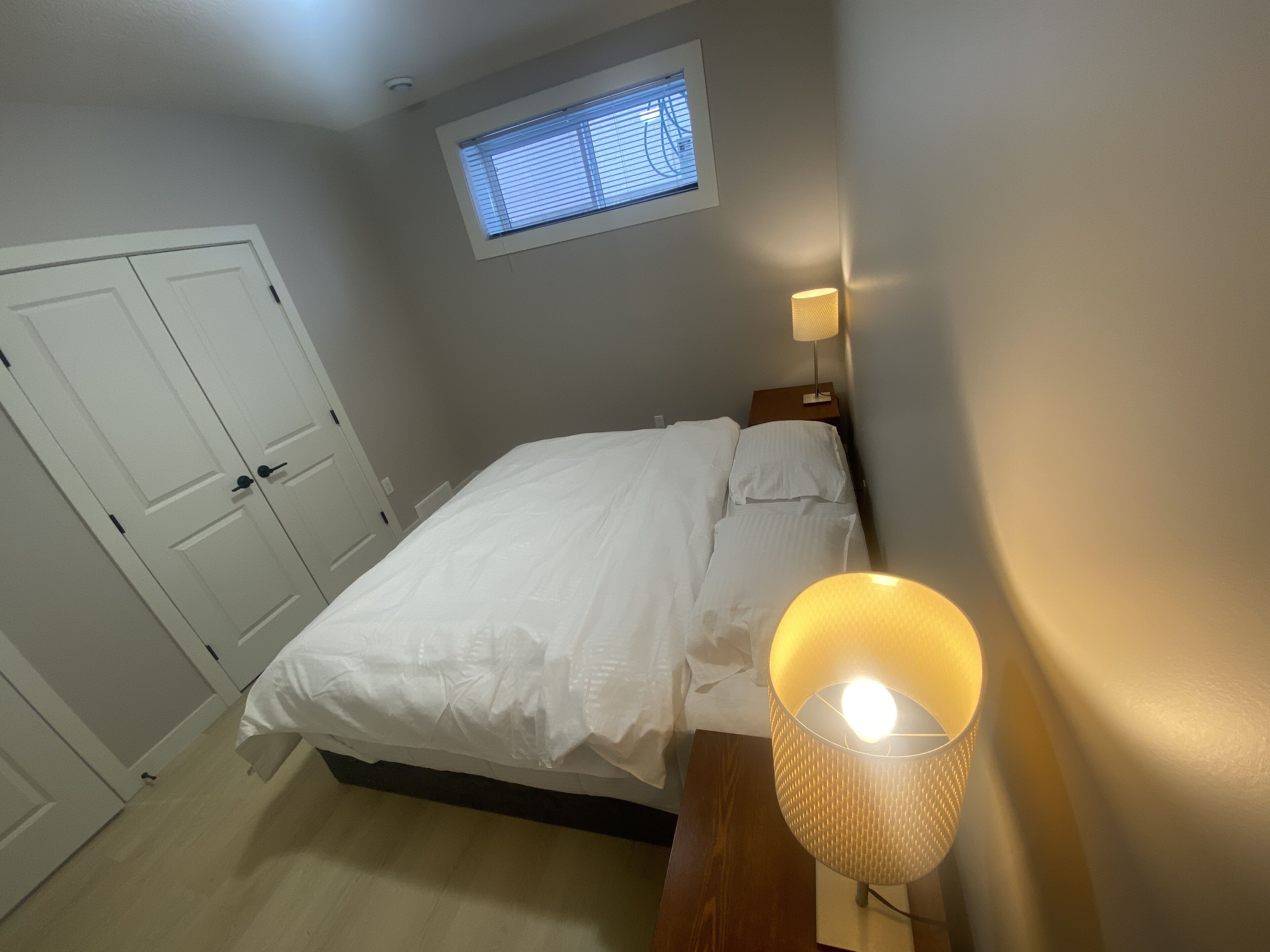 Une chambre à coucher avec un lit, une table de chevet, une lampe, une fenêtre et une porte.