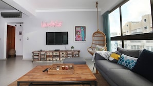 Uma sala de estar moderna com uma mesa de centro de madeira, sofá cinza e TV fixada na parede.