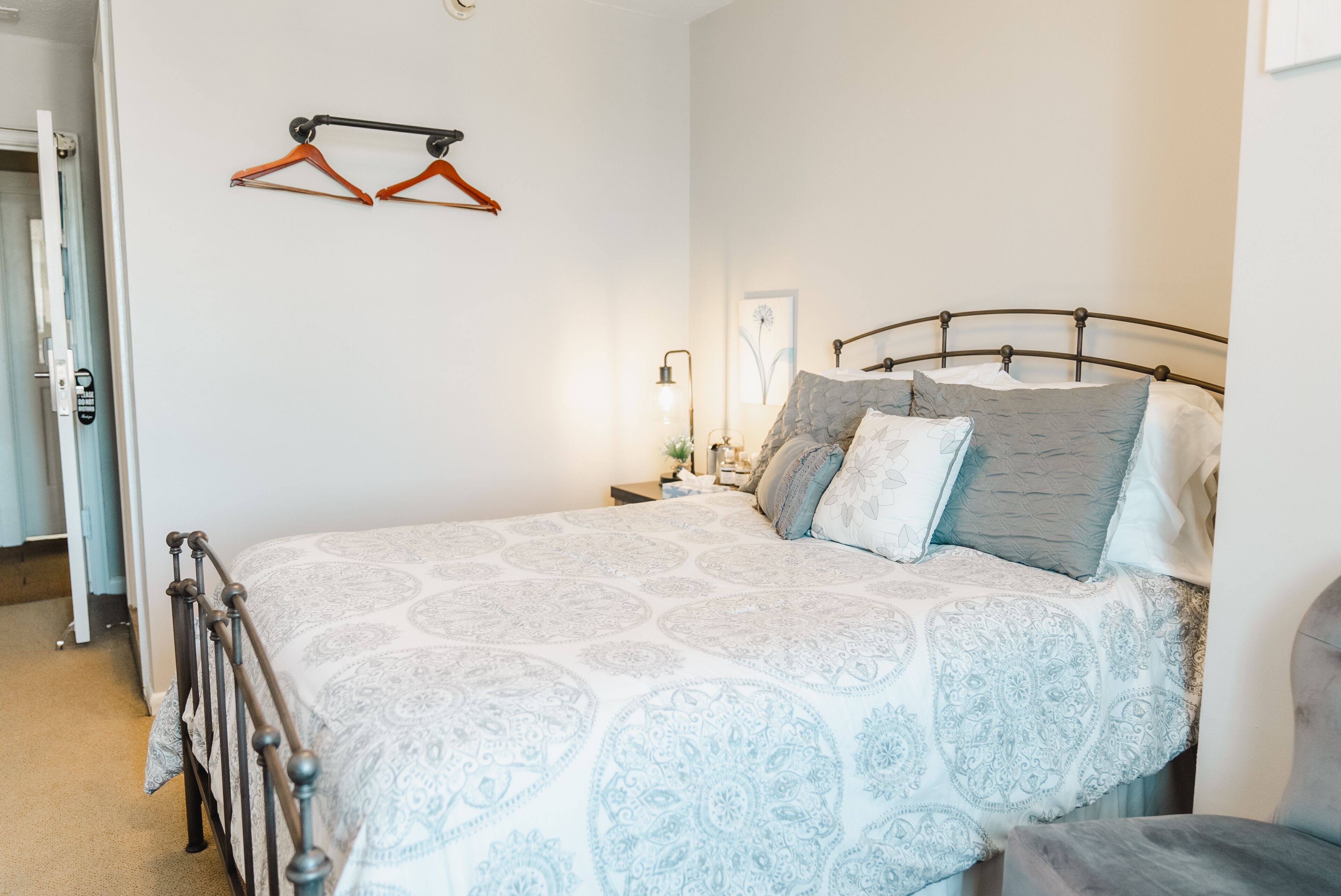Una cama bien hecha con una colcha estampada, una mesita de noche con una lámpara y un perchero de pared.