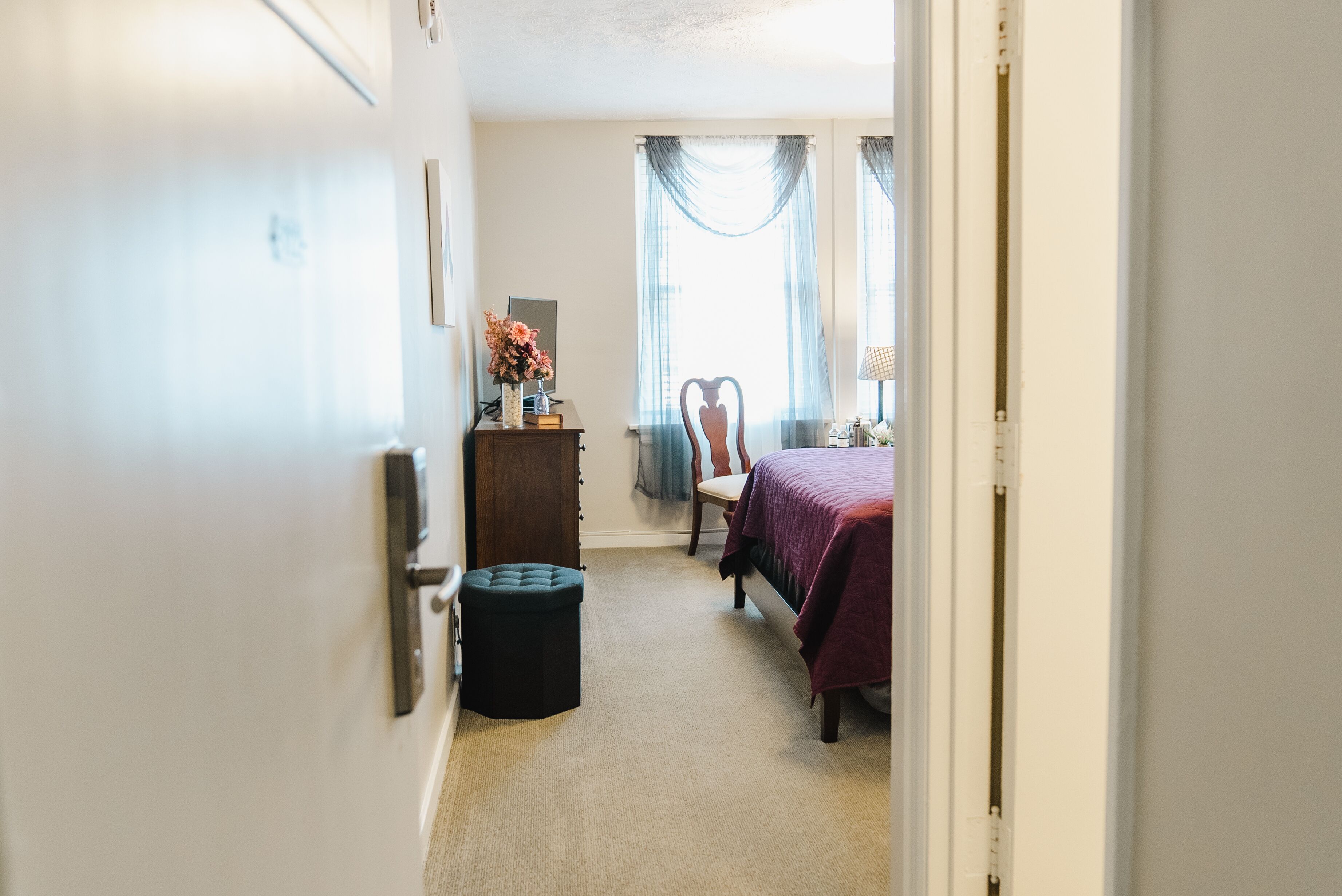 Une chambre à coucher avec un lit, une chaise, une commode et un petit tabouret.