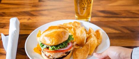 A plate with a burger and chips, a glass of beer, and a napkin on a wooden table.