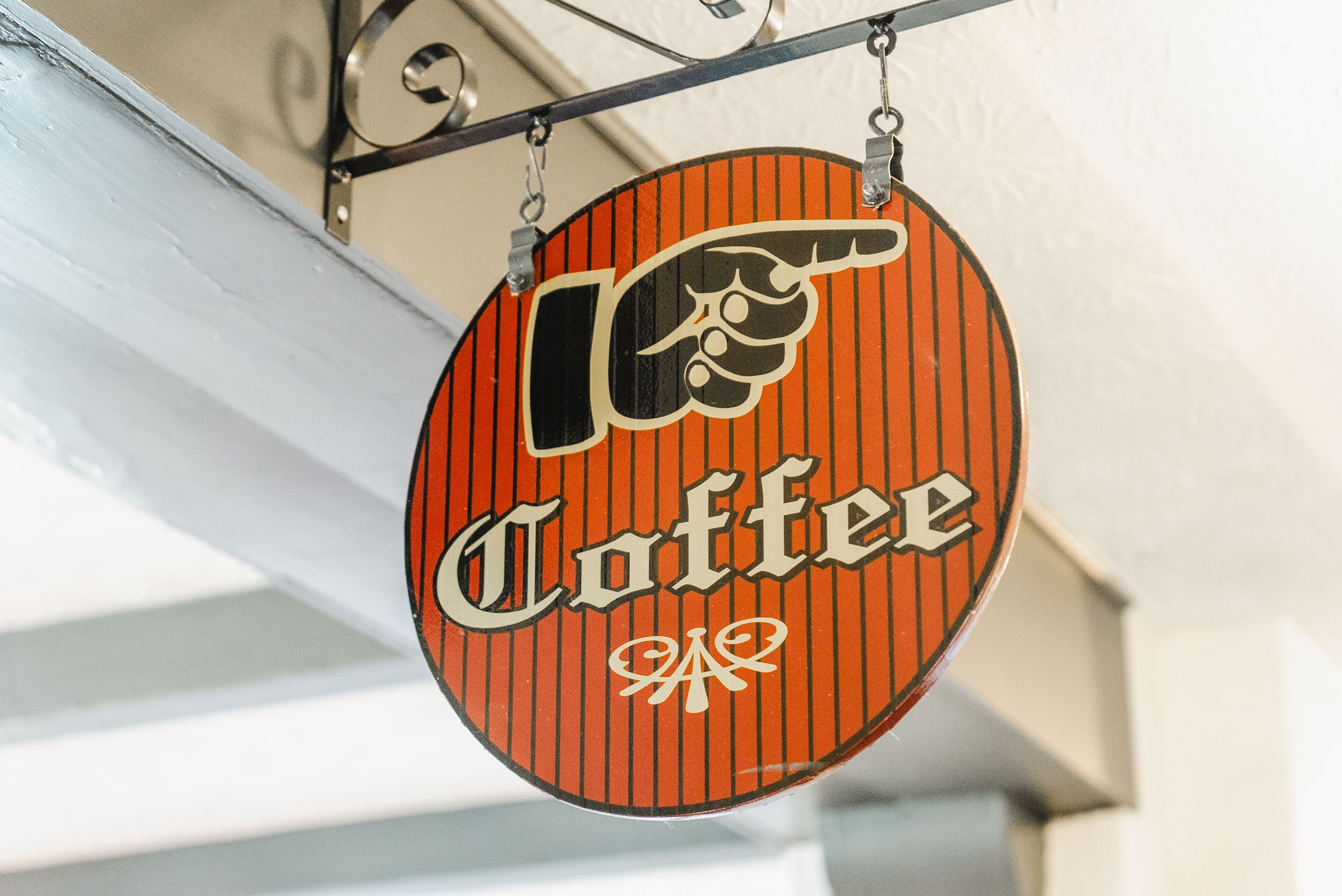 Un letrero circular con la palabra 'Coffee' y un gráfico de mano señalando, sujeto a un soporte metálico.