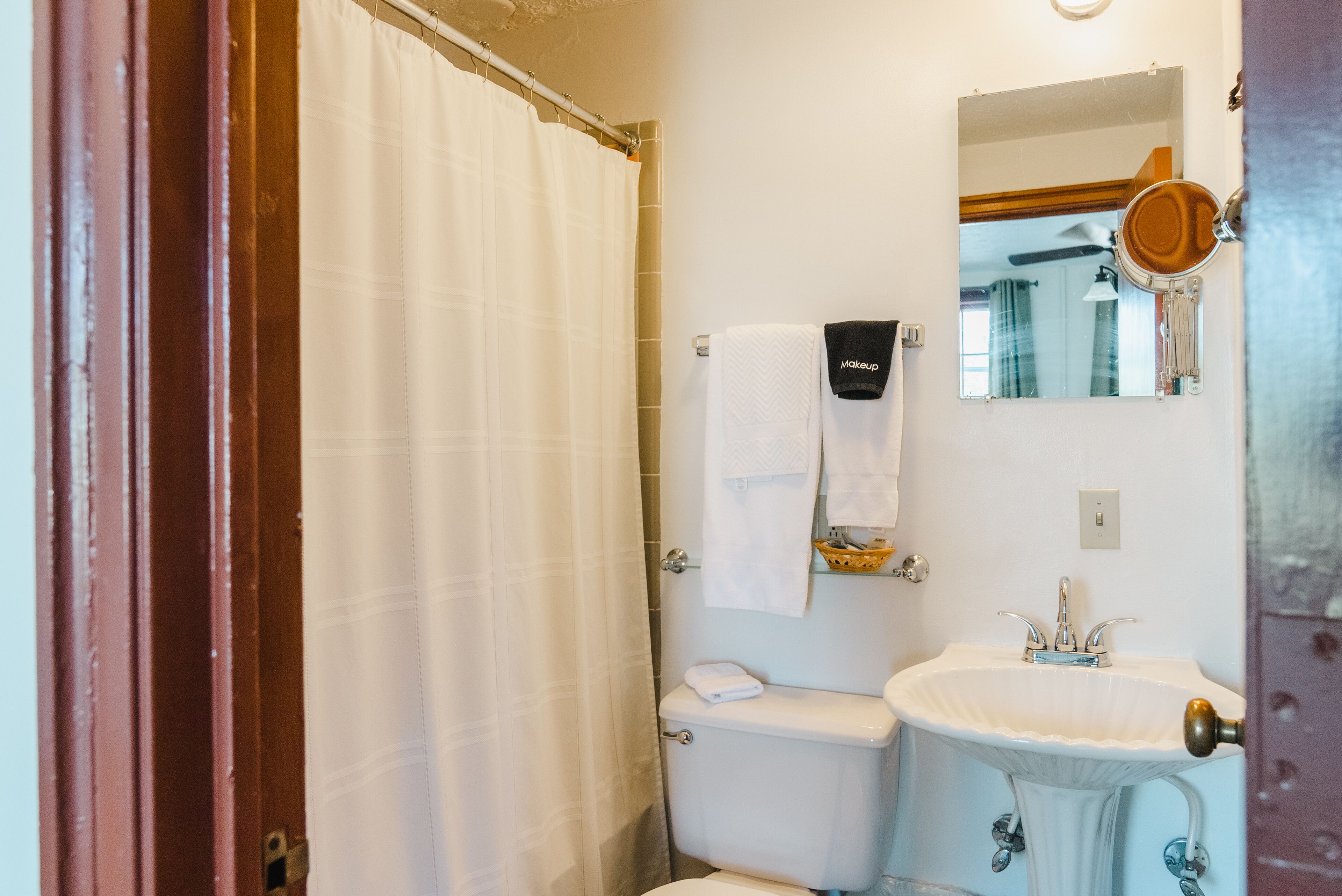 A bathroom with a white shower curtain, a white sink, and a mirror above the sink.