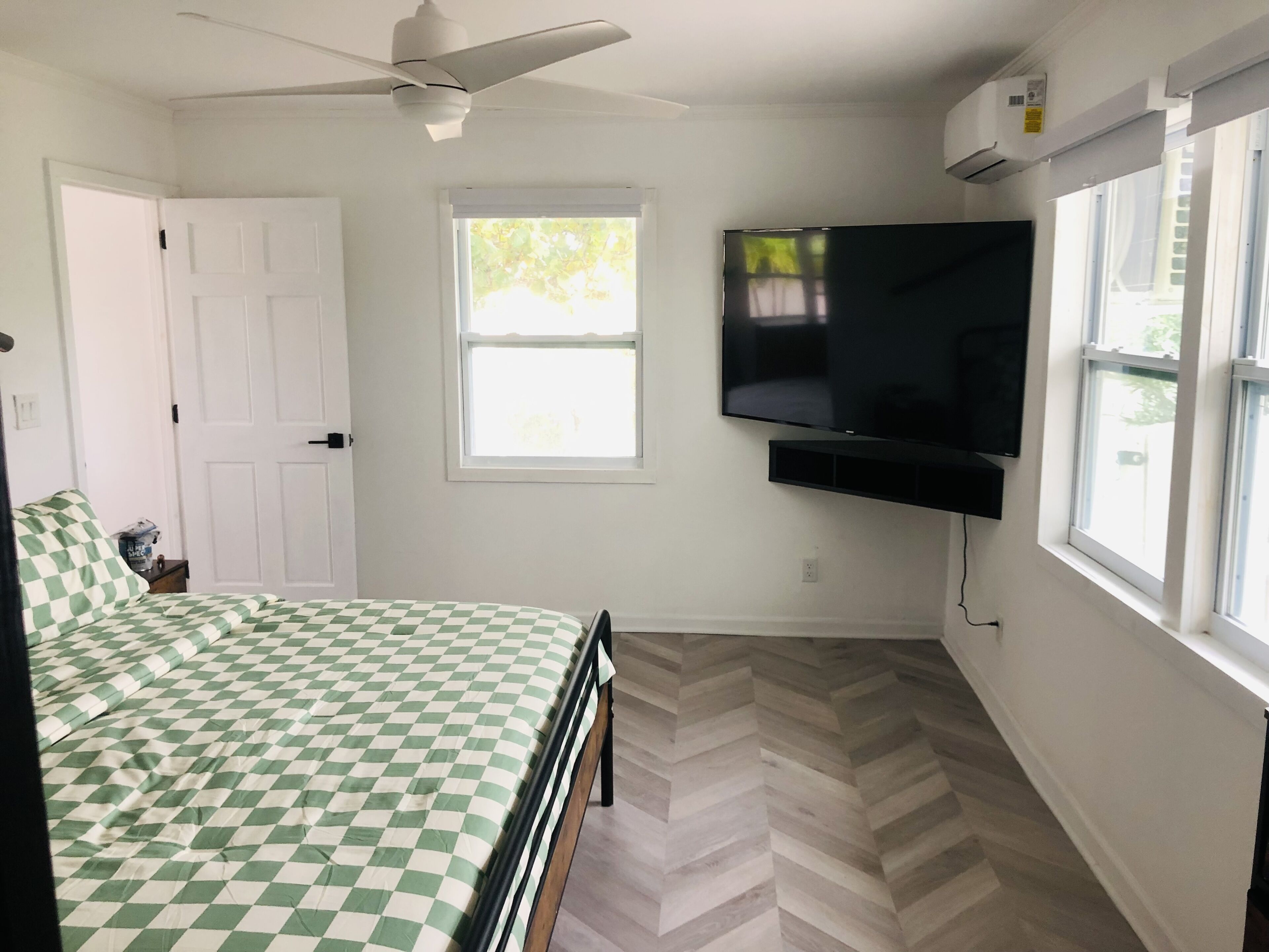 A bedroom with a bed, a ceiling fan, a window, and a mounted TV.