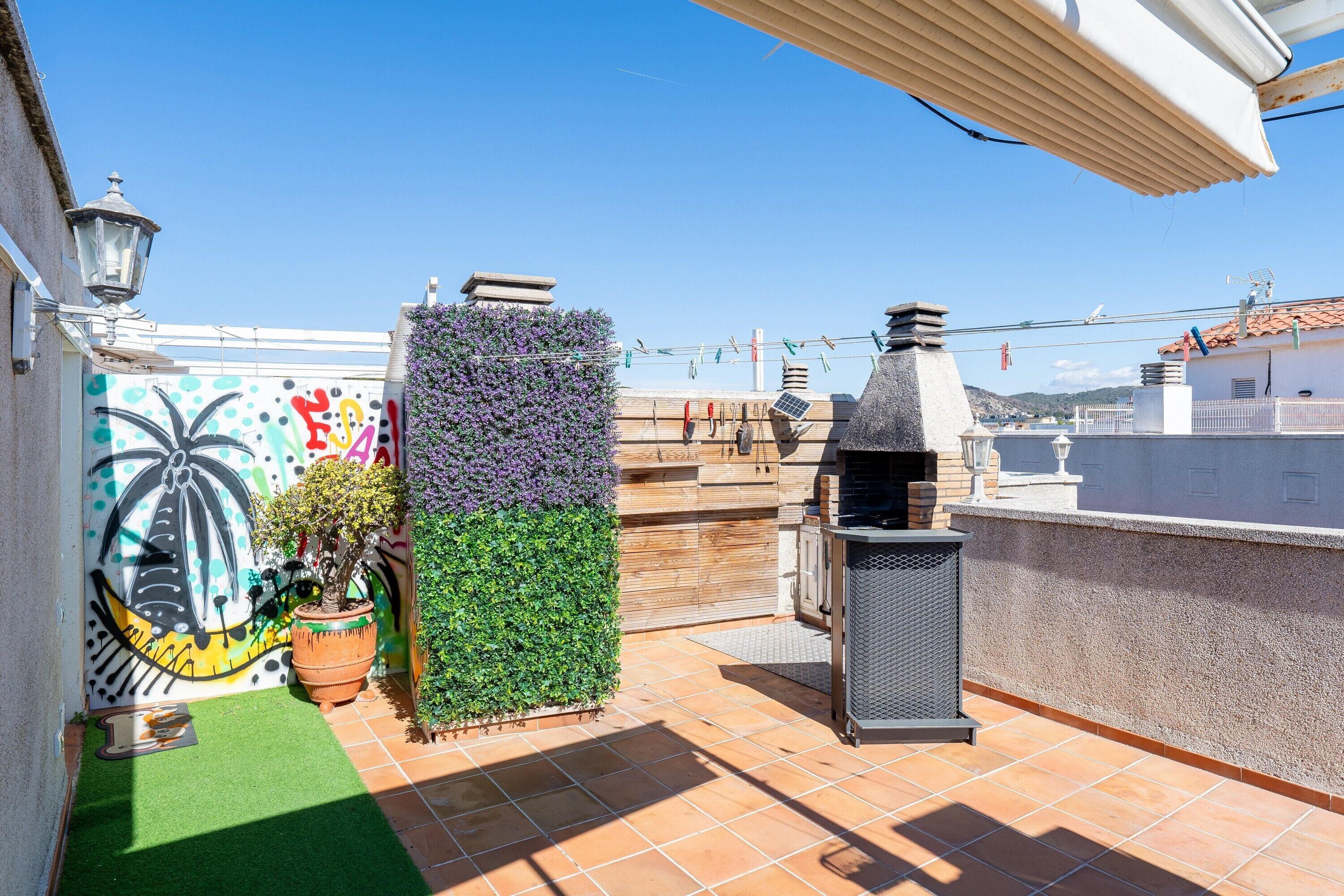 A rooftop terrace with a barbecue grill, potted plants, and a mural.