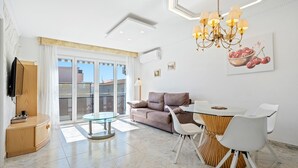 A modern living room with a sofa, dining table, chairs, a TV, and a large window. - Apartment with Private Terrace, Whirlpool, Wi-Fi and Air Conditioning (El vendrell)