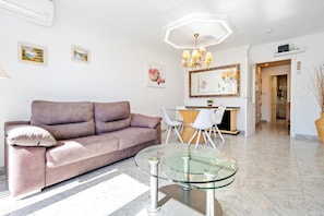 A modern living room with a sofa, glass table, and a dining area with chairs. - Apartment with Private Terrace, Whirlpool, Wi-Fi and Air Conditioning (El vendrell)
