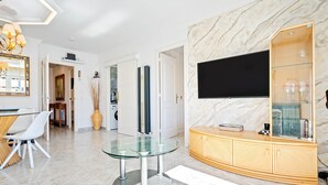 A modern living room with a glass table, a TV mounted on a marble wall, and a wooden cabinet with glass shelves. - Apartment with Private Terrace, Whirlpool, Wi-Fi and Air Conditioning (El vendrell)