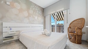 A modern bedroom with a large bed, a wicker chair, and a view through a glass door. - Apartment with Private Terrace, Whirlpool, Wi-Fi and Air Conditioning (El vendrell)