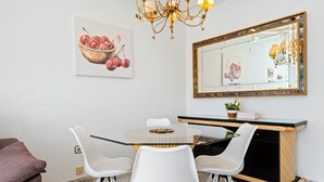 A dining area with a glass-top table, white chairs, a wooden cabinet, and a mirror with a decorative frame. - Apartment with Private Terrace, Whirlpool, Wi-Fi and Air Conditioning (El vendrell)