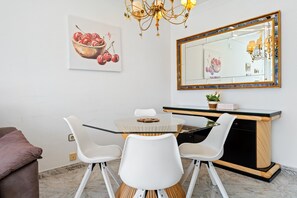 Un coin repas comprenant une table à plateau en verre, des chaises blanches, un buffet en bois et un miroir avec un cadre décoratif.