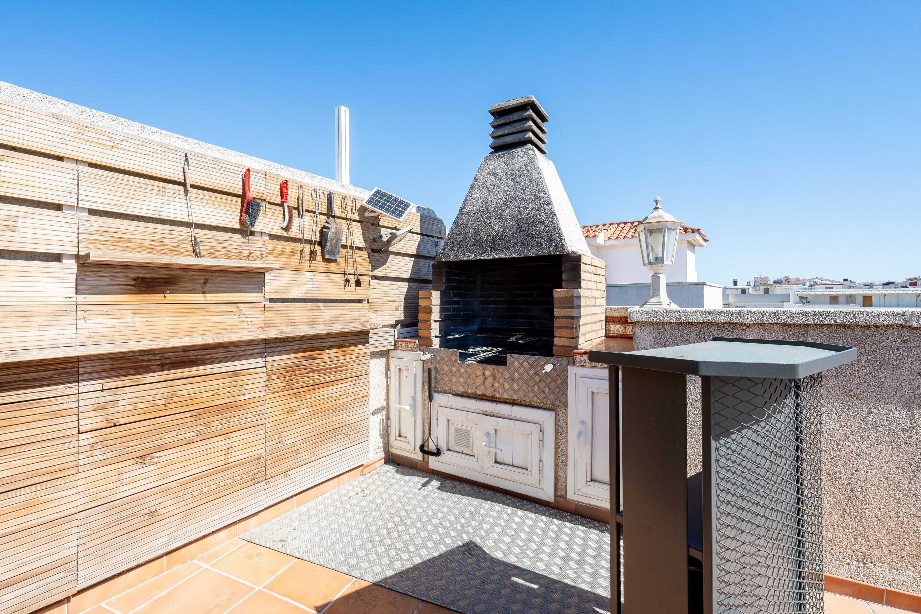 A rooftop patio with a wood-paneled wall, a stone chimney, and a metal grill.