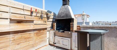 A rooftop patio with a wood-paneled wall, a stone chimney, and a metal grill.