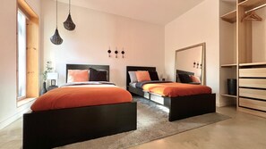 Quarto com duas camas, um espelho grande, um guarda-roupa e um lustre.