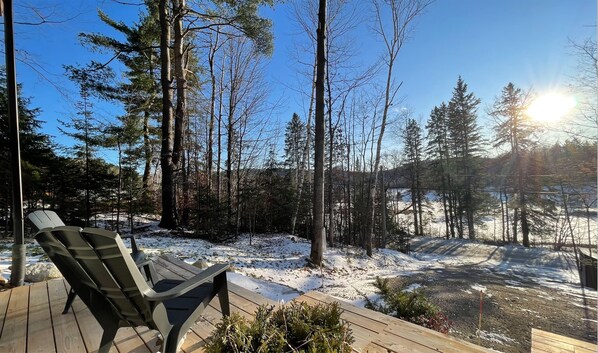 A deck with a chair, surrounded by a snowy forest with tall trees and a clear sky.