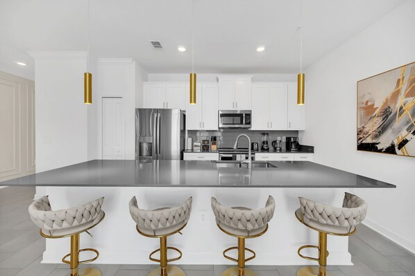 Una cocina moderna con armarios blancos, una isla grande y tres taburetes de bar.