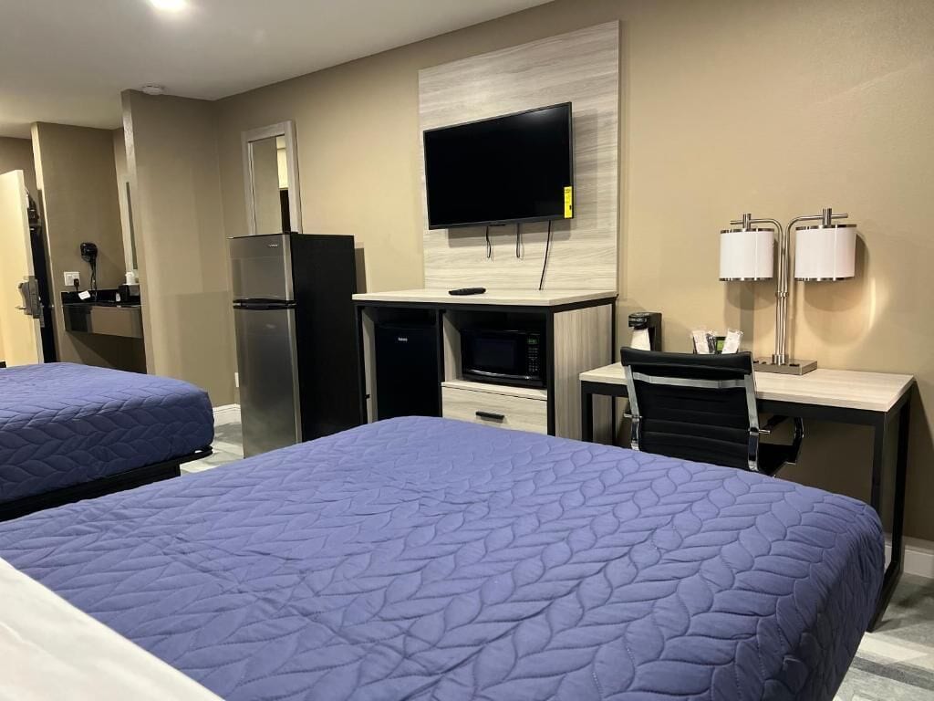 A hotel room with two beds, a desk with a computer, a flat-screen TV, and a refrigerator.