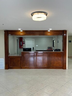 A reception area with a wooden reception desk, a chandelier, and a tiled floor. - Motel 6 Houma, LA (Houma)