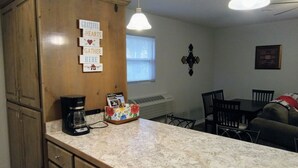 A kitchen with a marble countertop, wooden cabinets, a coffee maker, and a bulletin board with signs.