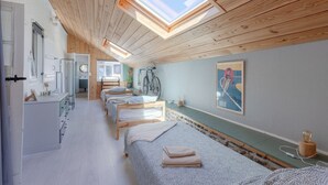Une pièce avec des poutres en bois au plafond, des lucarnes, un lit avec une tête de lit, une table de chevet, un miroir et un vélo fixé au mur.