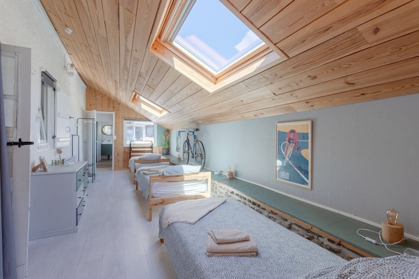 Una habitación con vigas de madera en el techo, tragaluces, una cama con cabecera, una mesita de noche, un espejo y una bicicleta fijada a la pared.