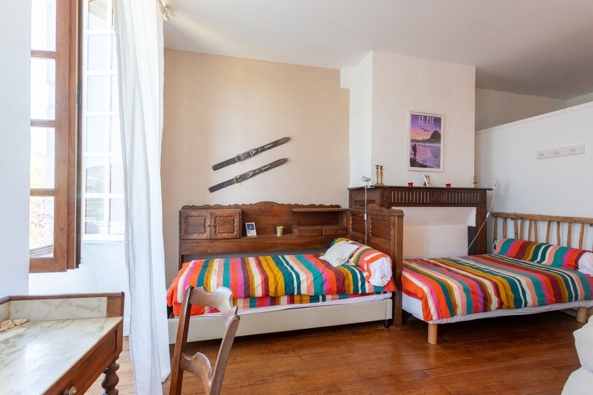 A room with two beds, a wooden desk, a chair, a fireplace, and a window.