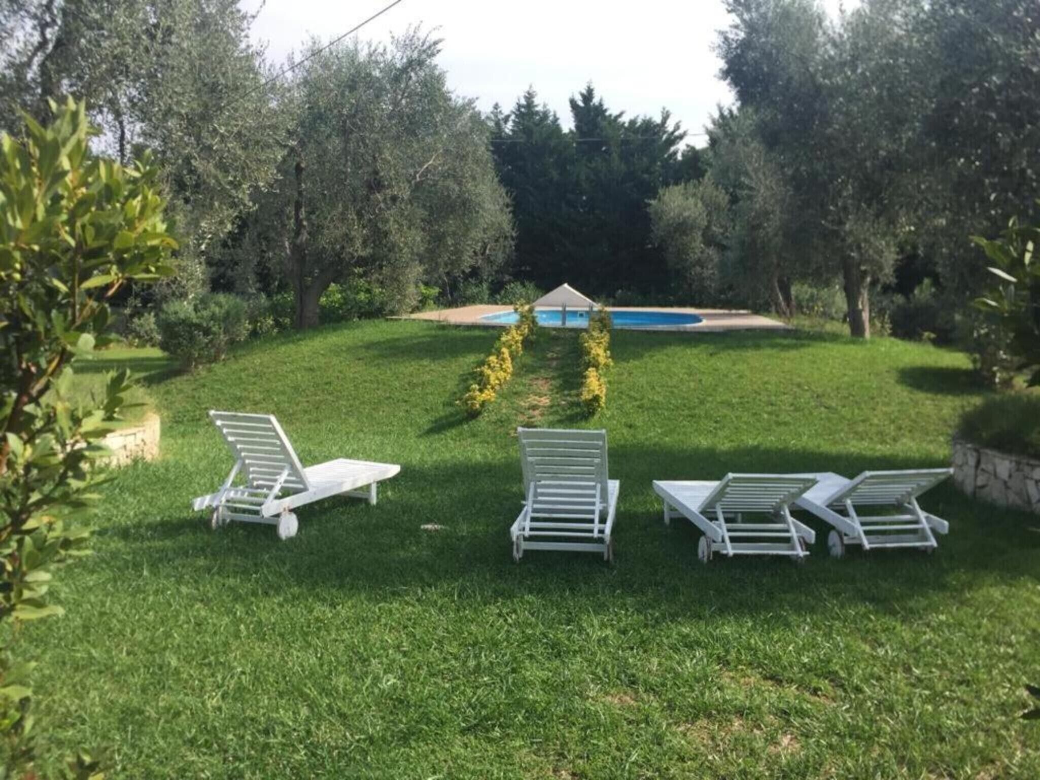 Un espacio al aire libre con césped y tres sillones blancos dispuestos en semicírculo.