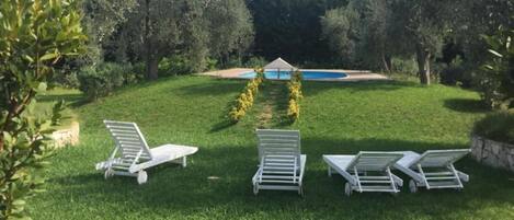 Un espacio al aire libre con césped y tres sillones blancos dispuestos en semicírculo.