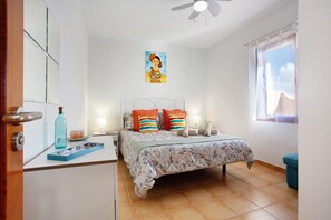 Une chambre à coucher avec un lit, une table de chevet, une fenêtre et un ventilateur de plafond.