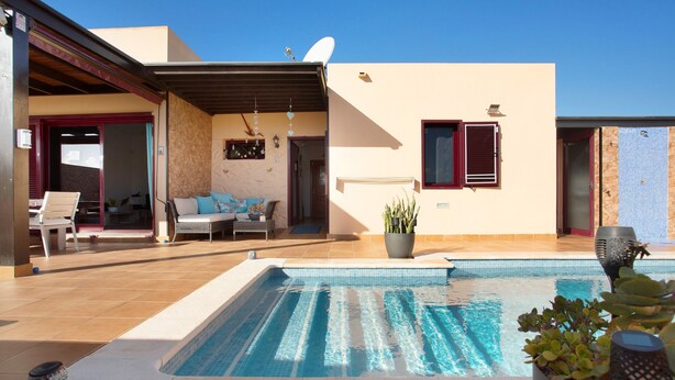 A swimming pool with a tiled deck, a patio area with outdoor furniture, and a building with a satellite dish. - Vacation Villa 'Amistad' with Private Pool, Private Terrace and Wi-Fi (Corralejo)