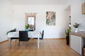 Un coin repas comprenant une table, des chaises, des plantes en pot, un tableau et un comptoir orné d’un vase et d’une carte.