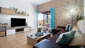 A modern living room with a flat-screen TV, a coffee table with decorative items, a sofa, and a brick-patterned wall. - Vacation Villa 'Amistad' with Private Pool, Private Terrace and Wi-Fi (Corralejo)