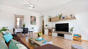 A living room with a sofa, a coffee table, a TV, a dining area with chairs, and a ceiling fan. - Vacation Villa 'Amistad' with Private Pool, Private Terrace and Wi-Fi (Corralejo)