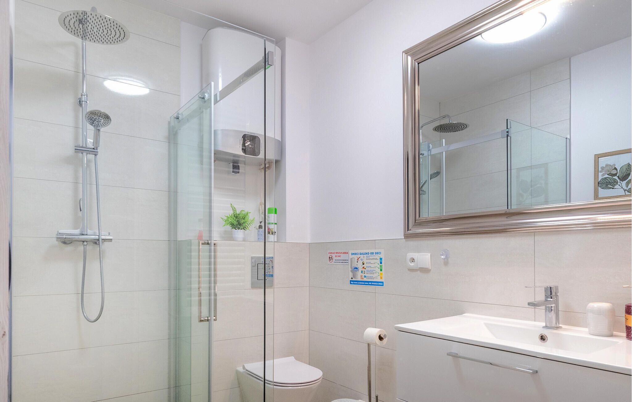 Une salle de bain moderne avec une douche à parois de verre, un grand miroir et un lavabo blanc.